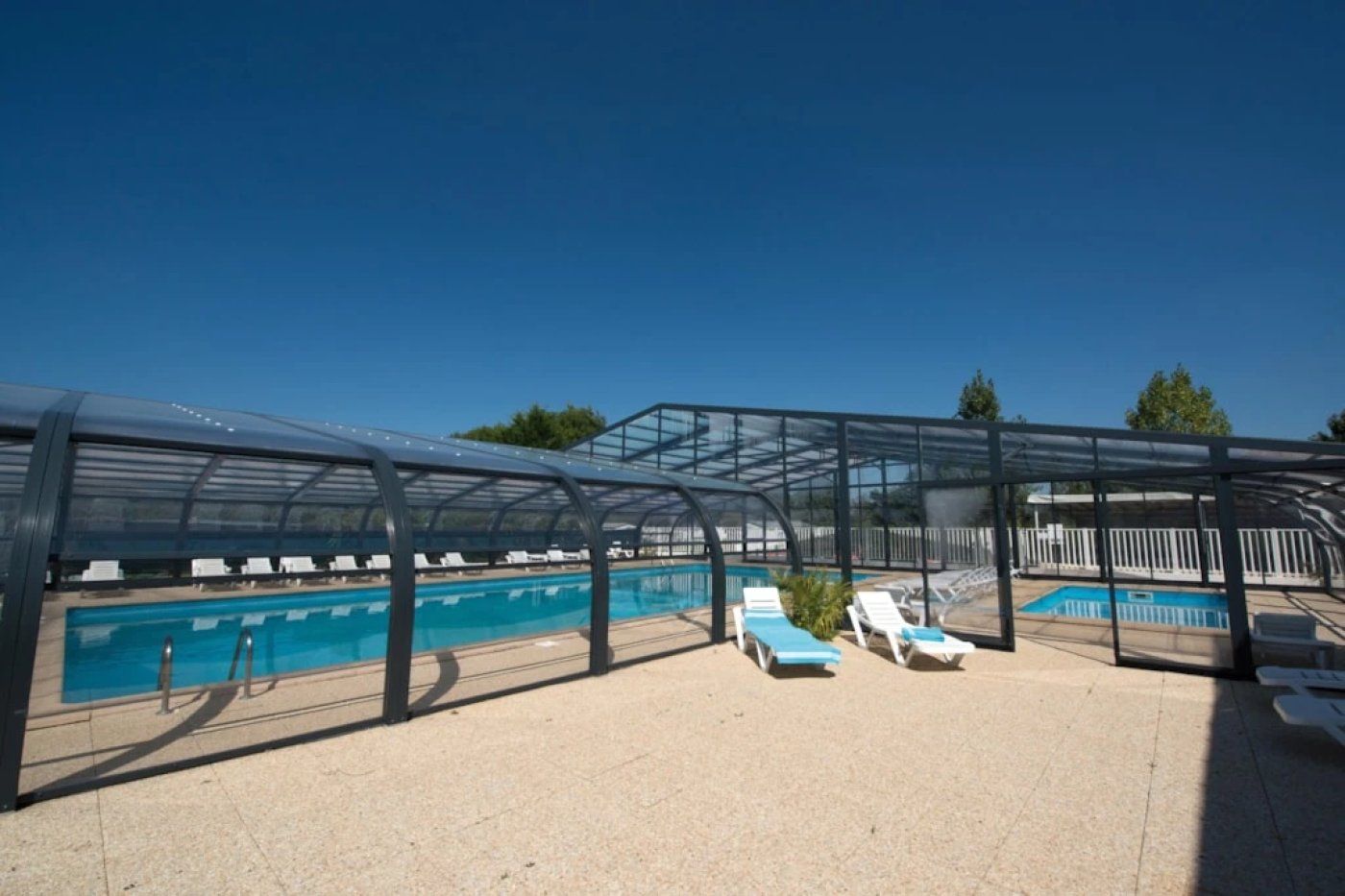 A covered outdoor swimming pool area with lounge chairs and a glass enclosure.