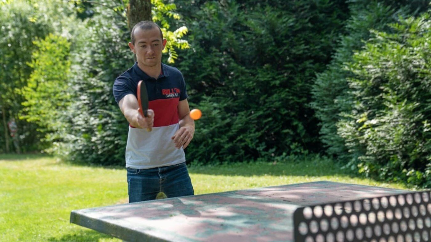 A person playing ping pong outdoors with a table and a ball.