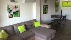 A modern living room with a sectional sofa, a dining table with chairs, and a kitchen area in the background. - Magnifique Appartement  VUE MER et MONTAGNES (Ghisonaccia)