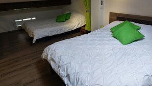 A room with two beds, each with white bedding and green pillows. There is a window with a view of the outside, and the room has wooden flooring. - Magnifique Appartement  VUE MER et MONTAGNES (Ghisonaccia)