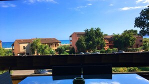 A table with chairs and a bowl, overlooking a beach and buildings. - Magnifique Appartement  VUE MER et MONTAGNES (Ghisonaccia)