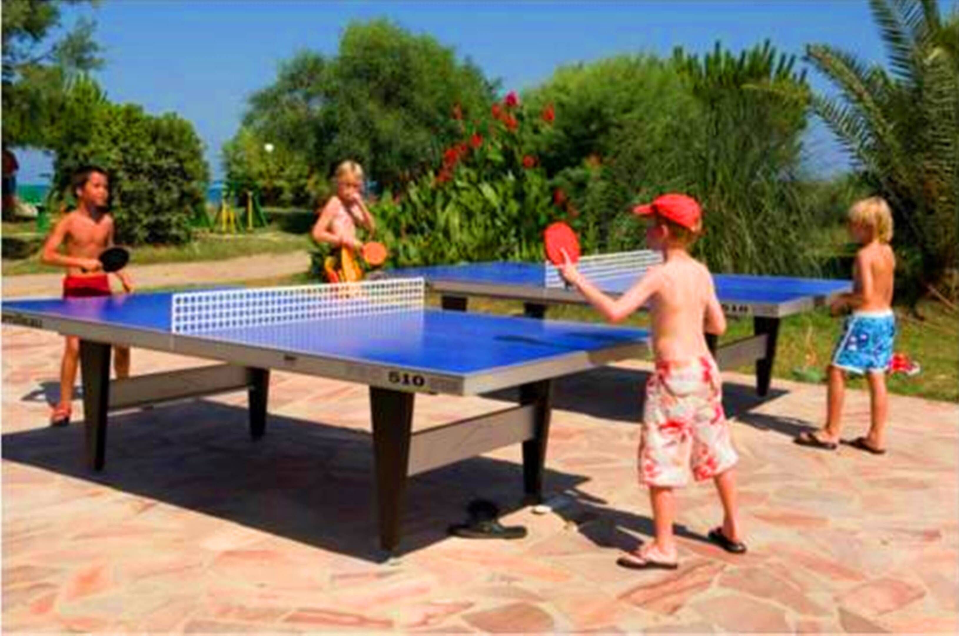 A table tennis table outdoors with a net in the middle, surrounded by greenery and a clear sky.