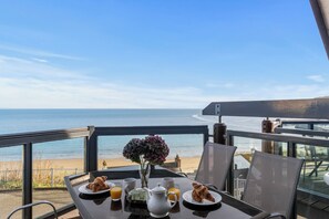 A table with breakfast items and a vase of flowers, overlooking a beach. - The Chandlery - Spectacular Sea Views, Parking (Saundersfoot)
