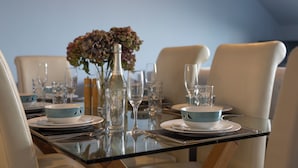 A dining table set with plates, bowls, glasses, and a vase with flowers. - The Chandlery - Spectacular Sea Views, Parking (Saundersfoot)