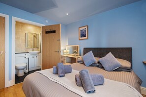 A bedroom with a bed, pillows, a bedside table, and a bathroom visible through an open door. - The Chandlery - Spectacular Sea Views, Parking (Saundersfoot)