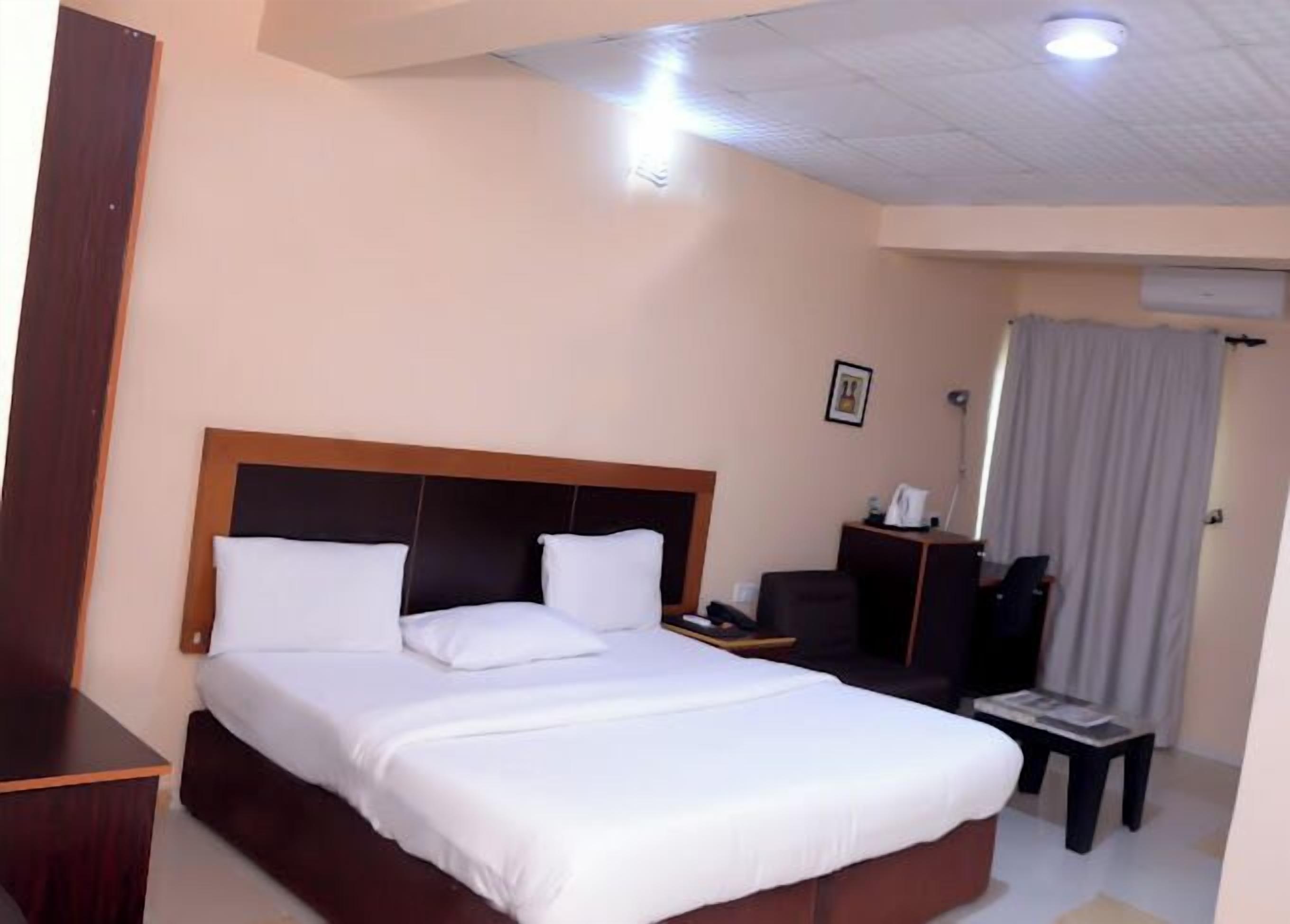 A hotel room with a large bed, a desk, a chair, and a window with curtains.