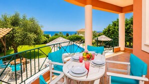 Ein Balkon mit Esstisch, mit Blick auf einen Swimmingpool und das Meer.