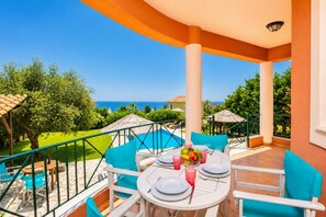 A balcony with a table set for dining, overlooking a swimming pool and the sea.