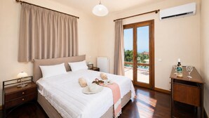 A bedroom with a bed, bedside tables, a nightstand, an air conditioner, a window with curtains, and a view of the outdoors. - Ionian Blue - Three Bedroom Villa, Sleeps 7 (Svoronata)