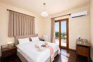 Ein Schlafzimmer mit Bett, Nachttischen, Klimaanlage, einem Fenster mit Vorhängen und Blick ins Freie.