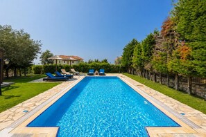 A rectangular swimming pool with a tiled edge, surrounded by a stone deck. There are lounge chairs along the poolside.