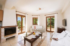 A spacious living area with a fireplace, a sofa, a dining table set with plates and a bottle, and a TV on a wooden stand.