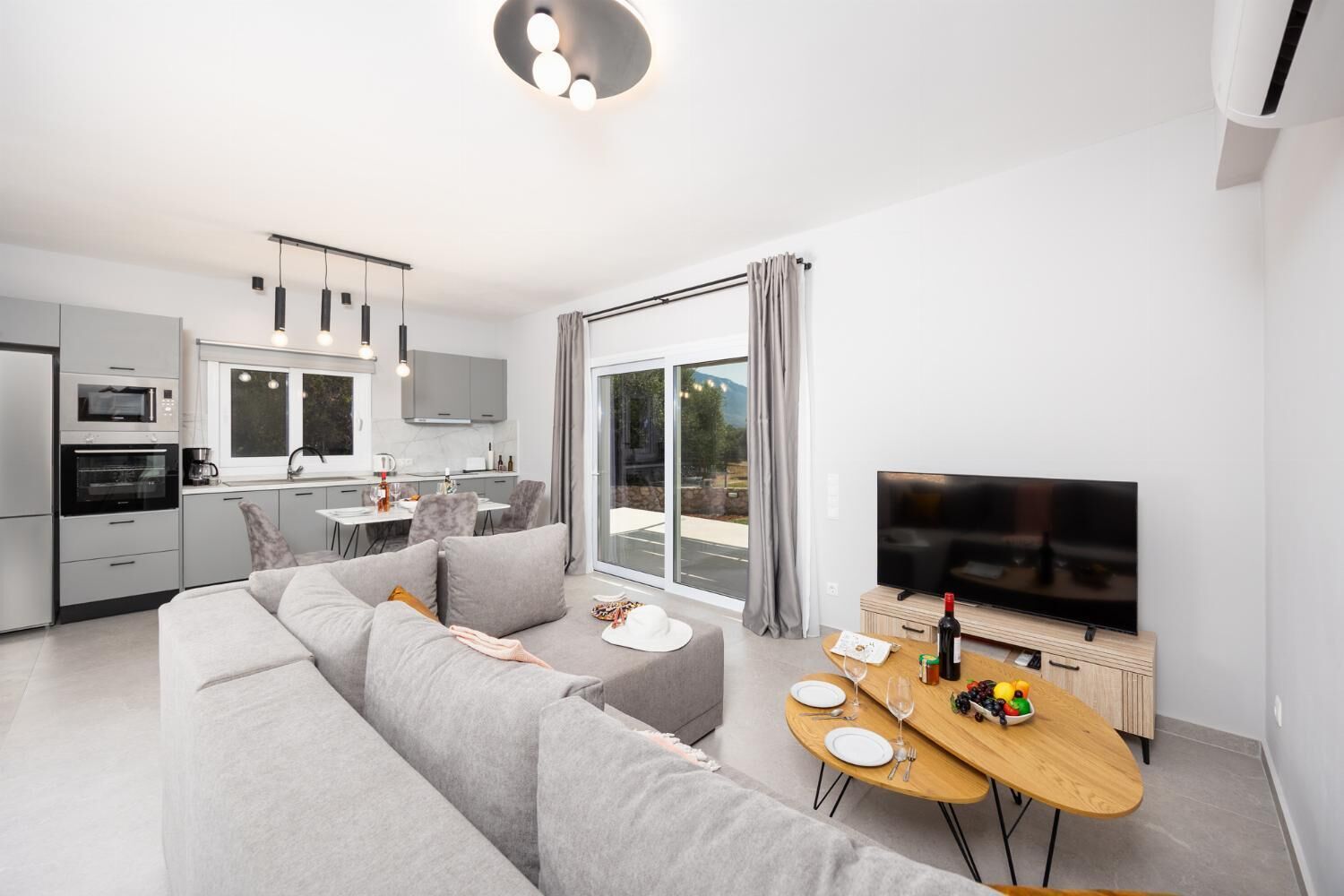 Een modern appartement met een woonkamer, eethoek en keuken. Er is een groot raam met gordijnen, een flatscreen televisie en een bank.