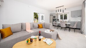 Ein modernes Wohnzimmer mit grauem Sofa, einem Essbereich mit Tisch und Stühlen sowie einer Küche im Hintergrund.