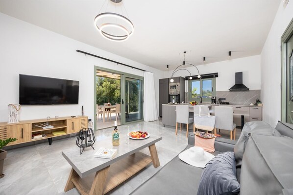 Ein modernes Wohnzimmer mit Flachbildfernseher, einer Holzunterhaltungsecke, einem Essbereich mit Tisch und Stühlen sowie einer Küche mit Herd und Spüle.