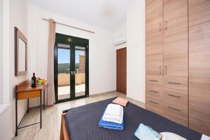 Ein Schlafzimmer mit Bett, Schreibtisch, Kleiderschrank und einer Glastür zum Balkon.