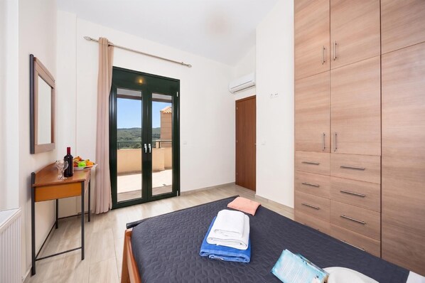 Un dormitorio con cama, escritorio, armario y puerta corrediza de vidrio a un balcón.