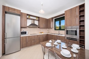Cocina moderna con armarios de madera, horno integrado, microondas y comedor para cuatro.