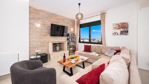 A modern living room with a fireplace, a sofa, a coffee table, and a TV mounted on the wall. - Villa Olive - Four Bedroom Villa, Sleeps 7 (Gerani)