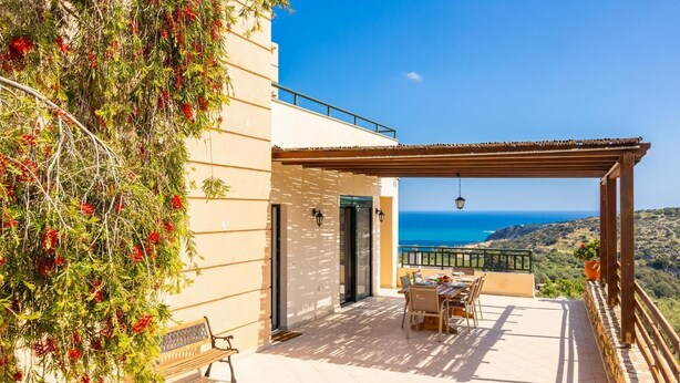 Eine Terrasse mit Tisch und Stühlen, einer Bank und Blick auf das Meer.