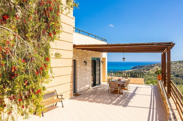 A terrace with a table and chairs, a bench, and a view of the sea.