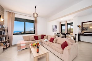 Een moderne woonkamer met een beige bank, een houten salontafel en een eethoek met uitzicht.