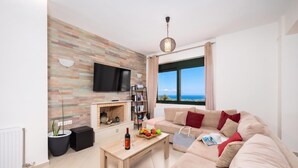 Ein Wohnzimmer mit Kamin, Fernseher, einer Couch und Meerblick.