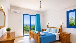 Een slaapkamer met een houten bed, een nachtkastje, een dressoir, een kamerplant, een balkon met uitzicht en een hanglamp.