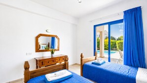 Een slaapkamer met twee bedden, een houten dressoir, een spiegel en uitzicht op een zwembad.