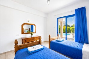 A bedroom with two beds, a wooden dresser, a mirror, and a view of a swimming pool.