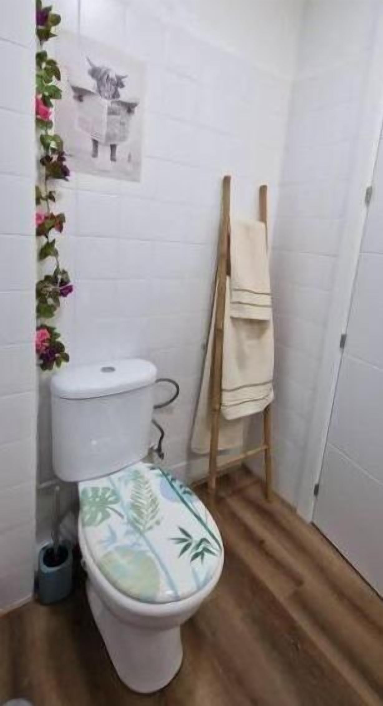 A small bathroom with a toilet, a wooden floor, and a towel rack.