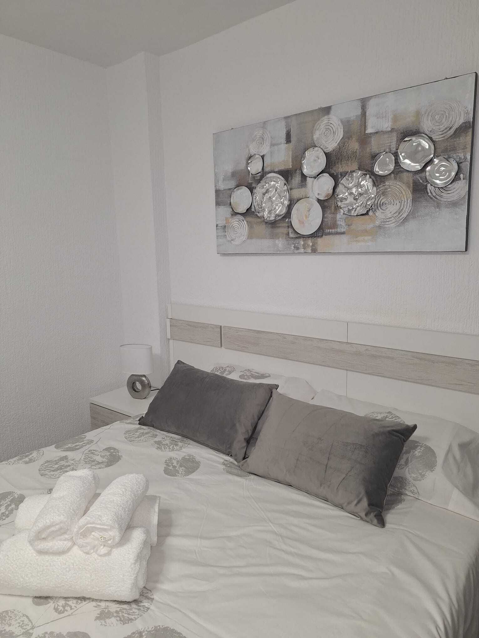 Una cama bien hecha con una colcha estampada con motivos florales, dos almohadas y una toalla doblada.