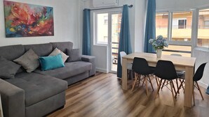 En moderne stue med en grå sofa, et træspisebord med sorte stole, et farverigt abstrakt maleri og udsigt til altanen.