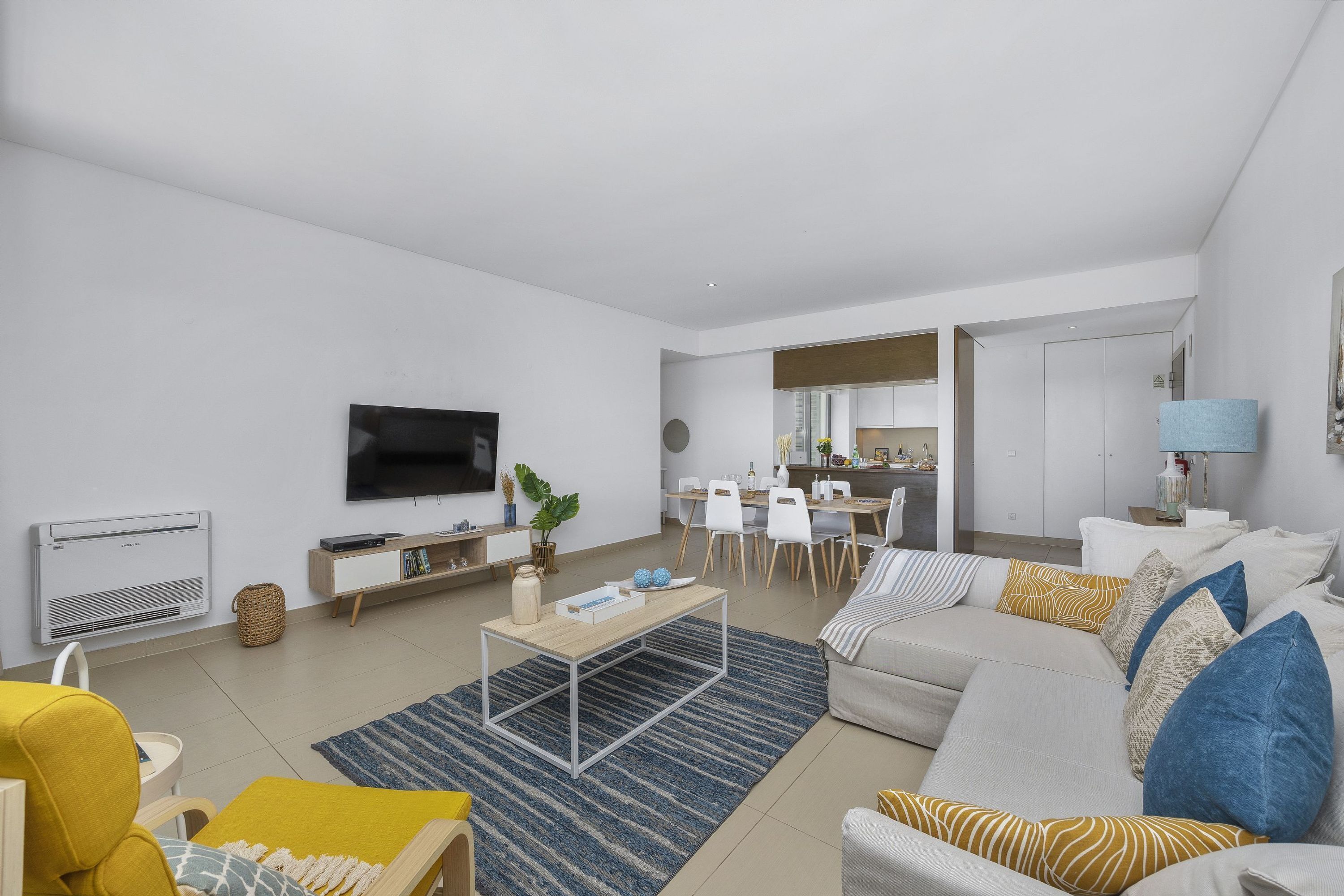 Una sala moderna con sofá, mesa de centro y televisor. Hay un comedor con sillas y una mesa.