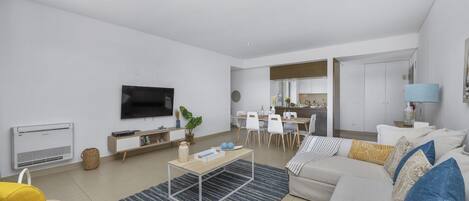 Una sala moderna con sofá, mesa de centro y televisor. Hay un comedor con sillas y una mesa.