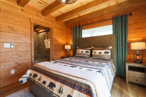 A wooden cabin bedroom with a large bed, two bedside tables, and a window with curtains. - 3 Bed | 4 Bath Mountain Escape in Wears Valley (Sevierville)