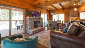 A spacious living room with a stone fireplace, wooden ceiling beams, and a cozy seating area with a leather couch and green armchair. - 3 Bed | 4 Bath Mountain Escape in Wears Valley (Sevierville)