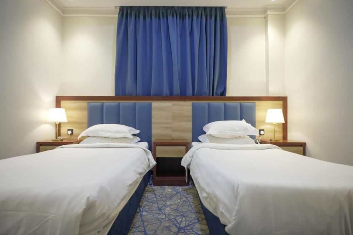 Ein Hotelzimmer mit zwei Betten, einem hölzernen Kopfteil und einem blauen Vorhang.
