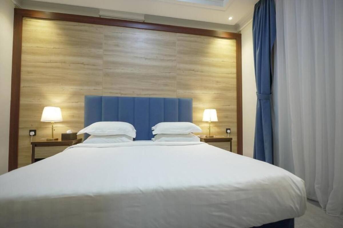 Ein Hotelzimmer mit einem großen Bett, zwei Nachttischlampen, einem Holzkopfteil und einem Fenster mit Vorhängen.