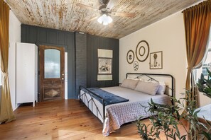 A bedroom with a bed, wooden floor, ceiling fan, and a door. - Historic Shotgun House/Walk To Town/Biking (Abita Springs)