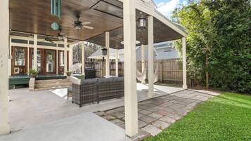 A covered patio area with outdoor seating, a pergola, and a view of a house in the background.