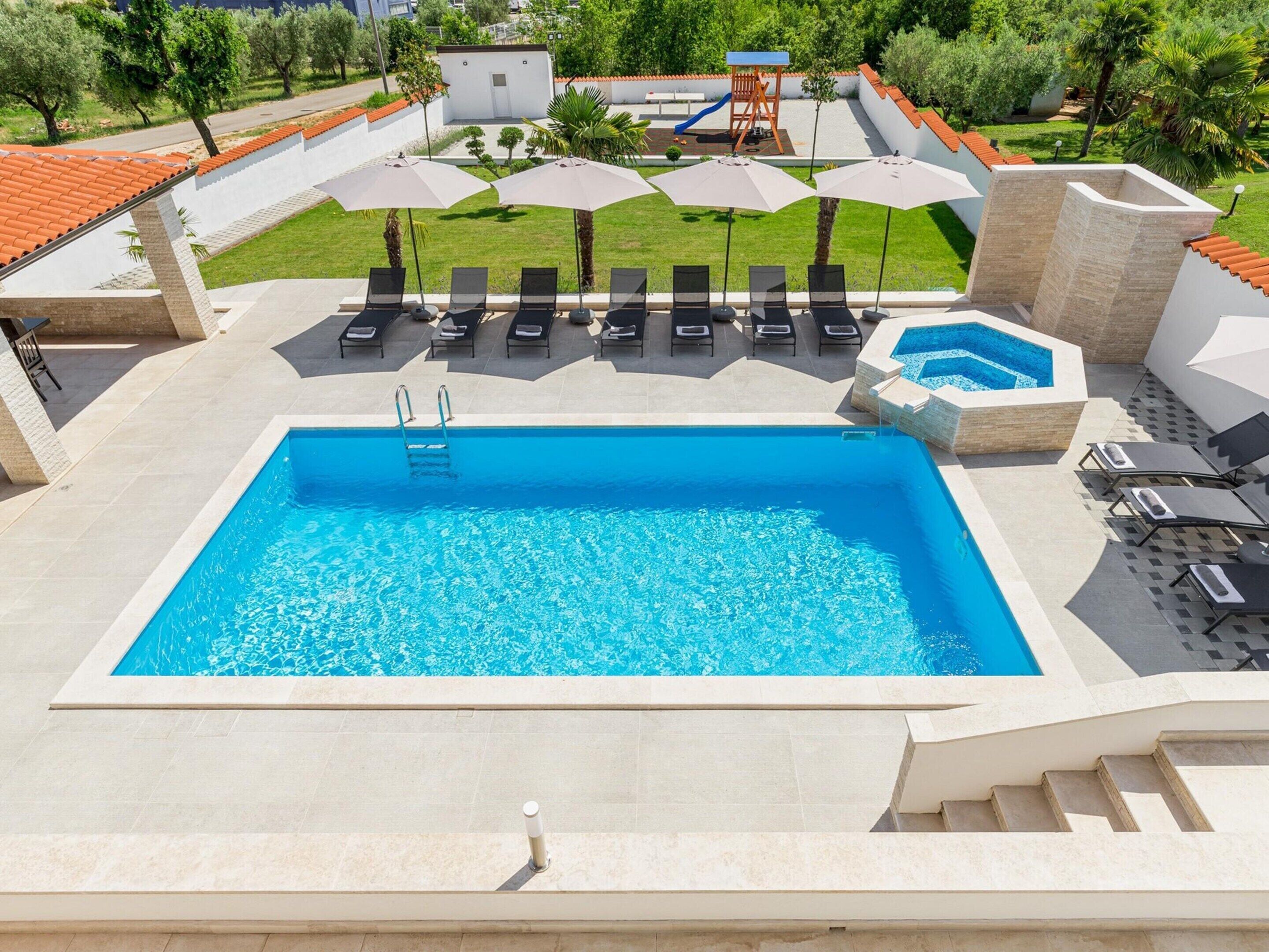 A rectangular swimming pool with a diving board, surrounded by lounge chairs and umbrellas.