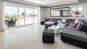 A modern living room with a large sliding glass door leading to an outdoor patio, a grey sectional sofa, a white coffee table, and a black ottoman.