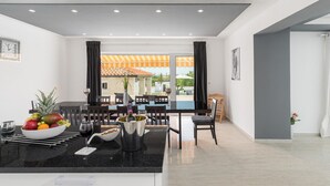 A modern dining area with a table set for two, a bowl of fruit, and a bottle of wine.