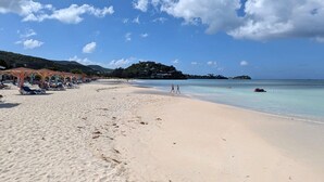 A beach with sun loungers and umbrellas, a clear sky, and a calm sea.