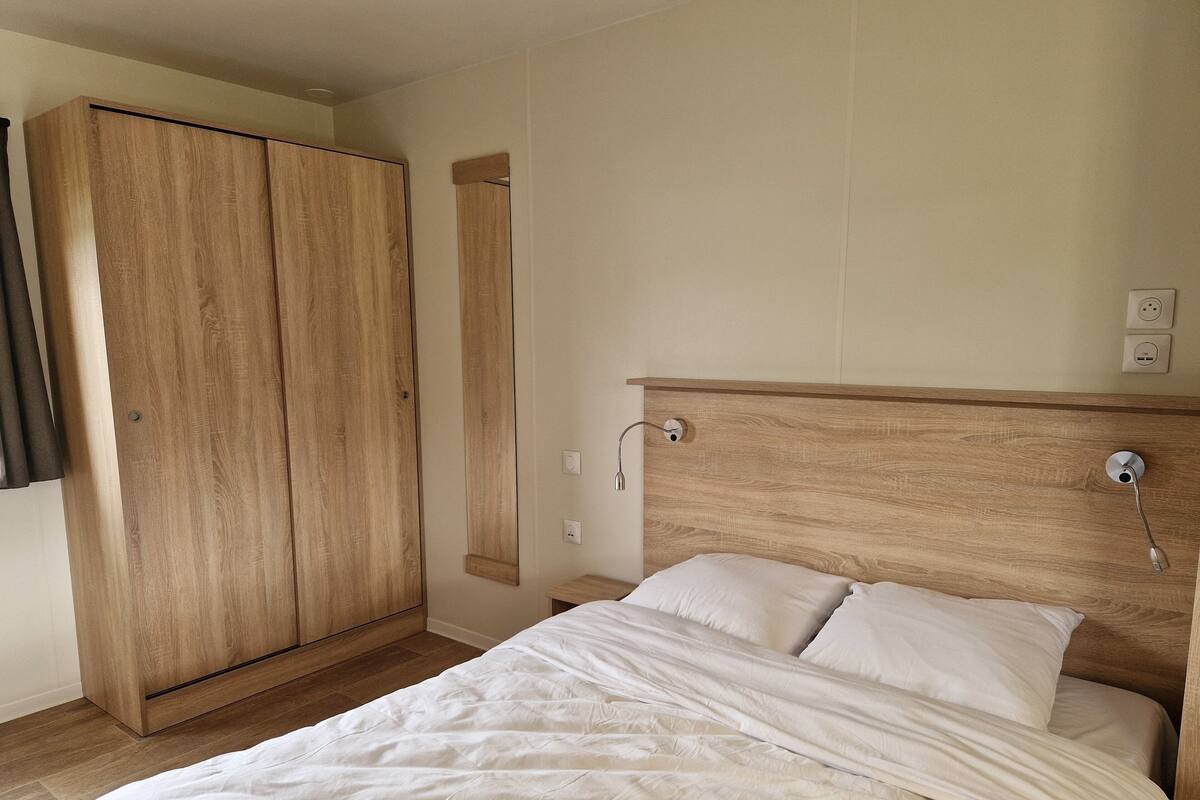 Un dormitorio con un armario de madera, una cama con ropa de cama blanca y una mesita de noche.
