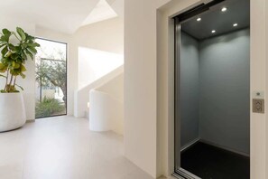 A modern interior with a large potted plant, a staircase, and a closed elevator. - Brand-New Quinta do Lago Villa Heated Pool&Jacuzzi (Almancil)