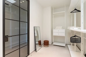 Un baño moderno con puerta de vidrio, un espejo, tocador blanco y un perchero.