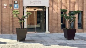 Das äußere Erscheinungsbild des Nova Roma Hotels mit freiem Eingang, einem Notausgangsschild und zwei Topfpflanzen davor.