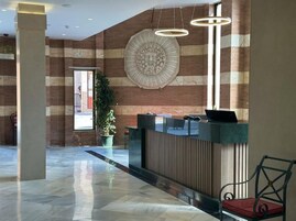 A reception area with a marble floor, a reception desk, a large decorative wall piece, and a potted plant.